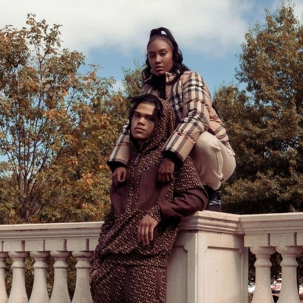 Two people sitting on a stone railing with trees and a clear sky in the background